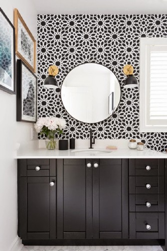 BLACK SCONCES TO A CONTEMPORARY HOME DESIGN Black and white bathroom with vase of flowers, small gallery wall, round mirror, black and gold wall sconces, and floral wall